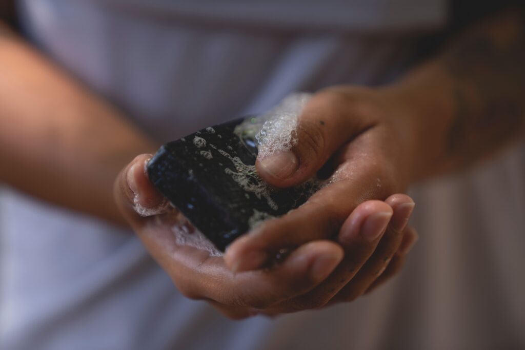 Detailed image of hands washing with black bar soap, capturing bubbles and texture.
