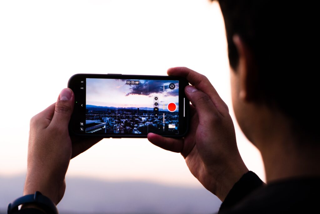 A person records a scenic sunset using a smartphone, capturing urban beauty.